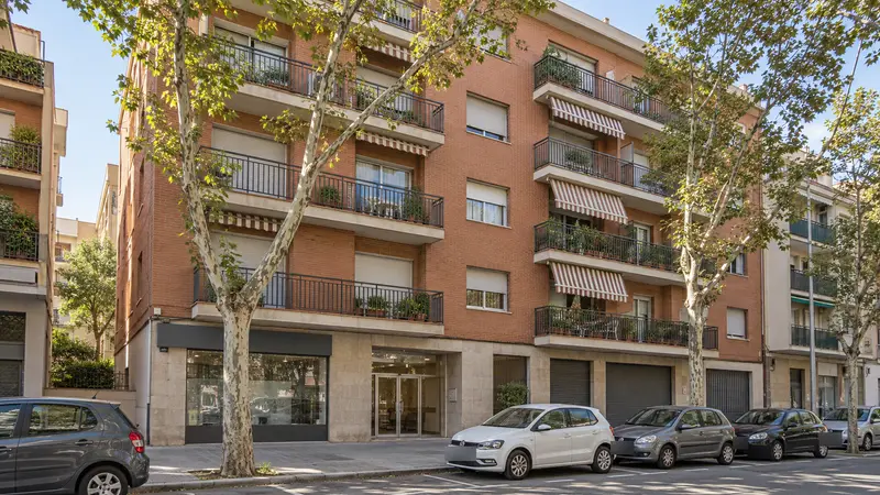 Edificio de viviendas de ladrillo con balcones y árboles en la acera