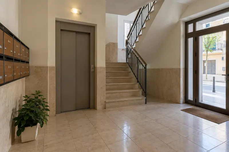 Vestíbulo de un edificio con ascensor, escalera y buzones