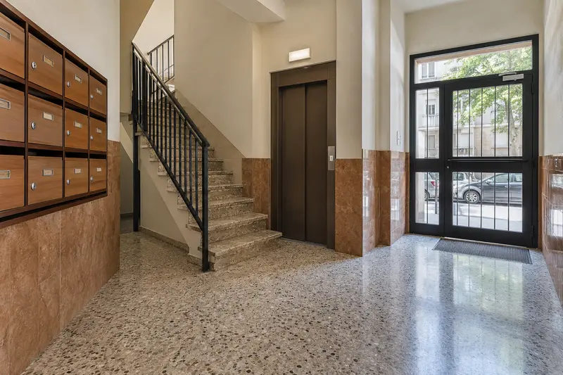 Vestíbulo de una comunidad con buzones, escalera y puerta de entrada