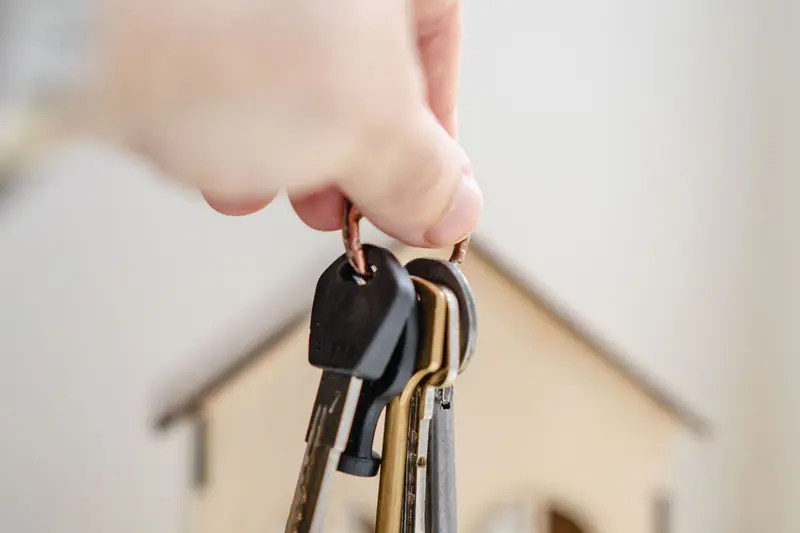 Mano con las llaves de una vivienda y una casa de madera al fondo
