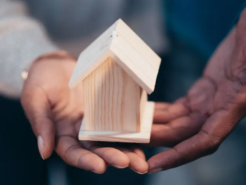 Manos sosteniendo una casa de madera, símbolo del seguro de hogar
