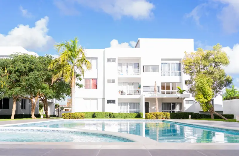 Urbanización de apartamentos blancos con piscina comunitaria y palmeras