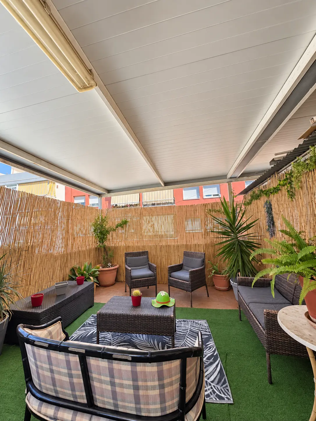 Terraza cubierta con sofás de mimbre, mesa baja y plantas