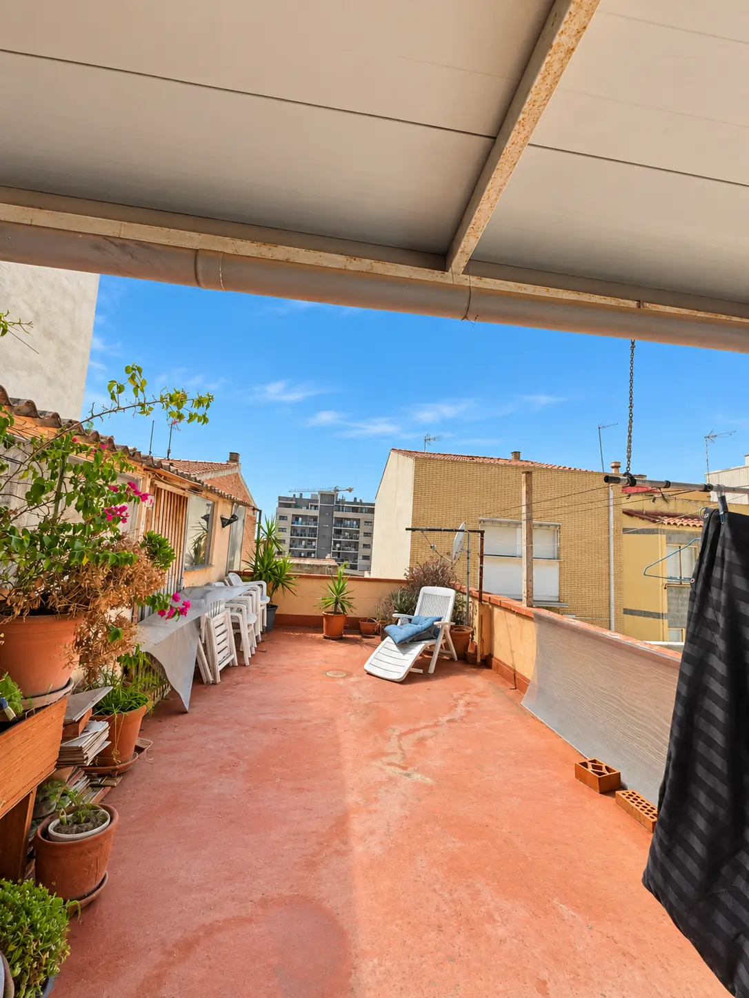 Parte descubierta de la terraza con suelo de barro, macetas y tumbona